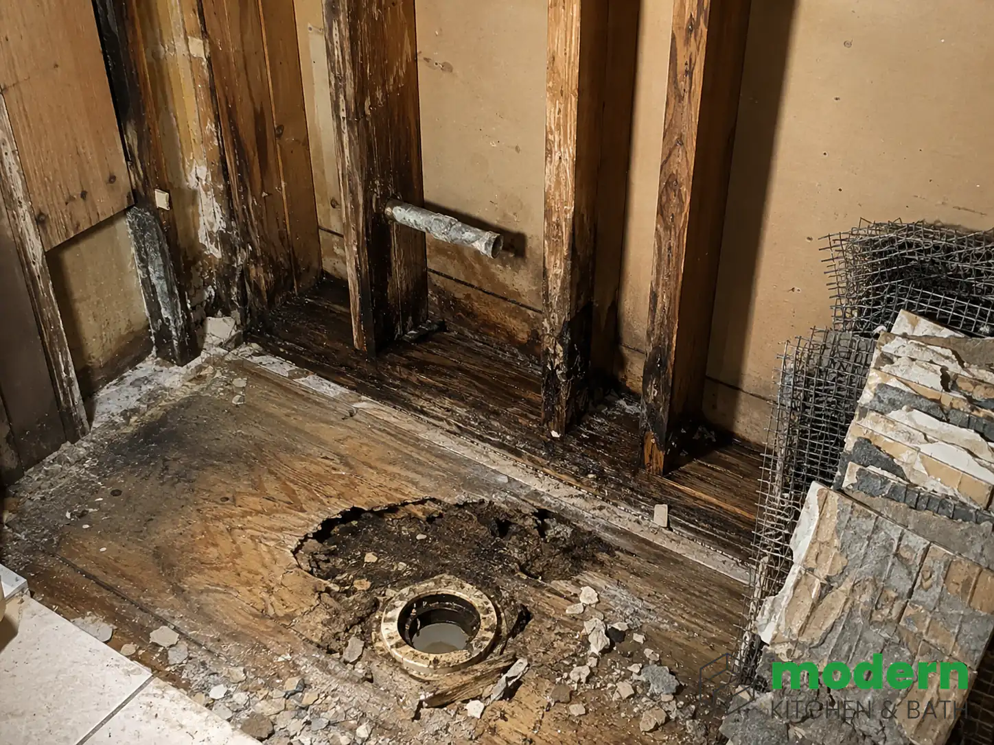 Bathroom demolition revealing water damaged subfloor and framing behind an old shower